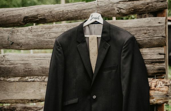 Blazer preto pendurado em um cabide, diante de uma parede de madeira