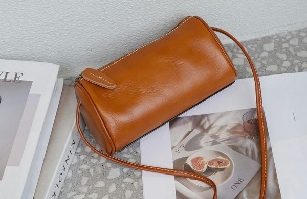 Bolsa transversal de couro caramelo em formato de cilindro, sobre revistas