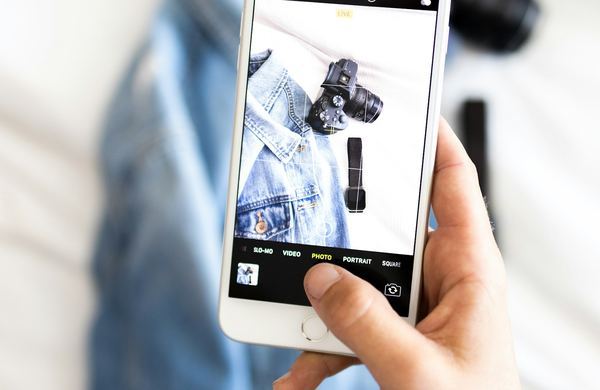 Mão segurando um celular com a câmera aberta, fotografando roupas