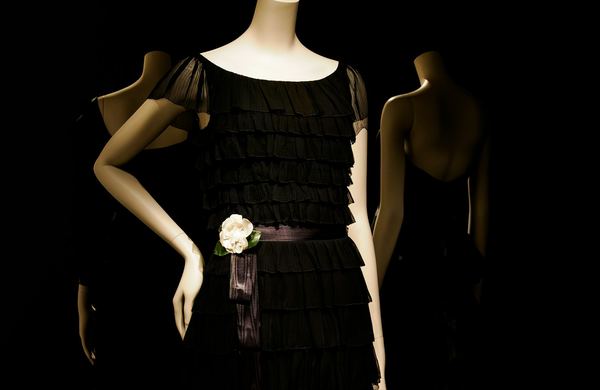 Vestido preto com babados em um manequim, com uma flor branca na cintura