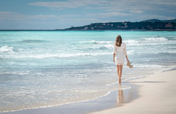 Mulher de vestido branco curto de renda caminhando na beira do mar